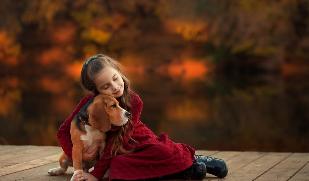 Маленькая девочка обнимает собаку породы бигль на мосту