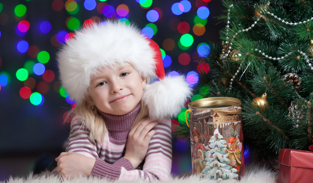 Маленькая девочка в новогодней шапке у елки