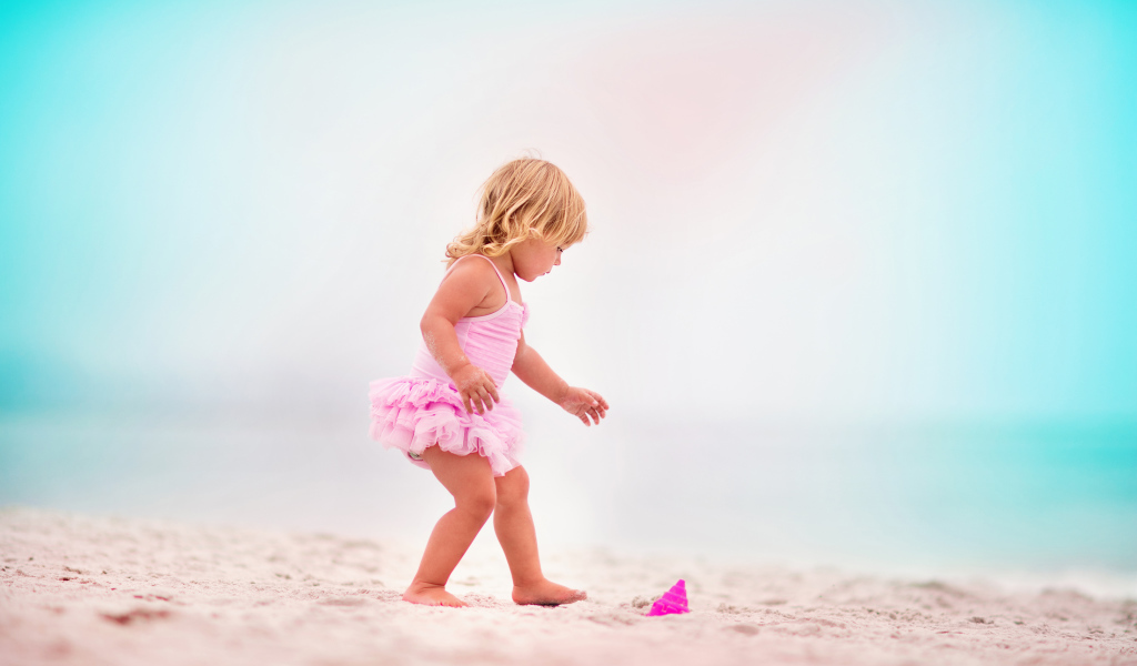 Маленькая девочка в розовом купальнике на песке