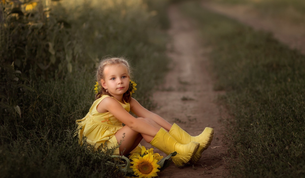Маленькая девочка в желтом платье сидит на земле с подсолнухами