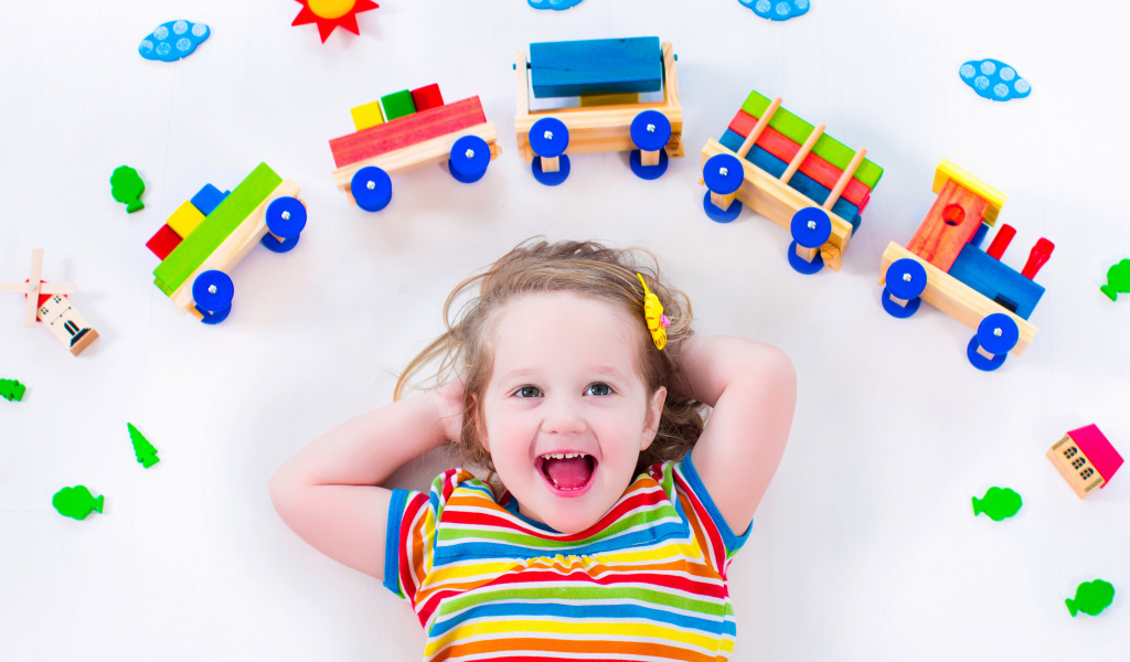 Маленькая девочка на сером фоне с игрушечным паровозом 