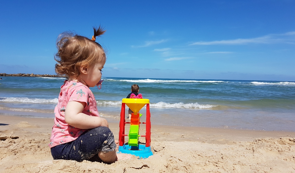 Маленькая девочка играет на песке у моря