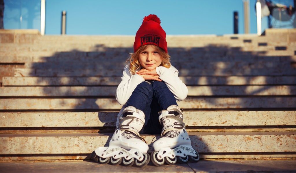 Маленькая девочка в роликах сидит на ступеньках 