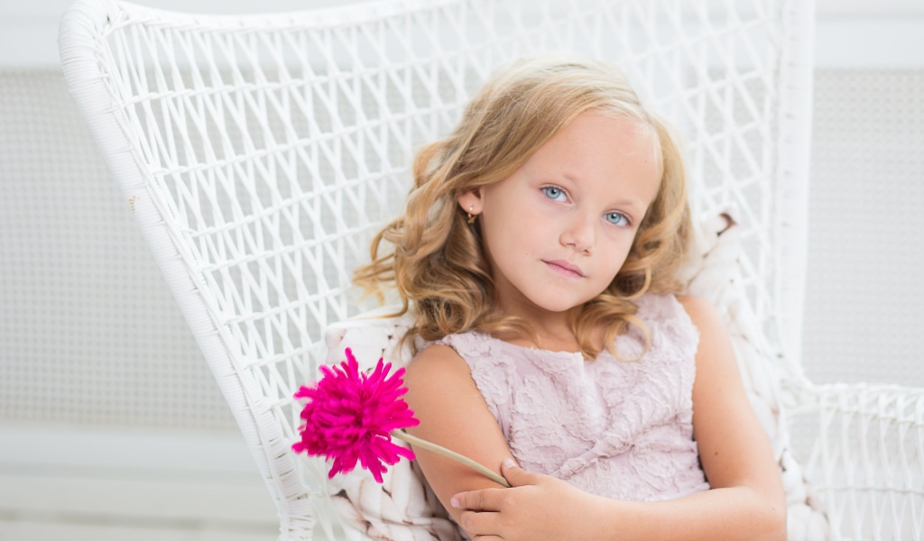 Маленькая девочка сидит в белом кресле с розовым цветком