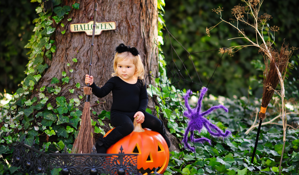 Маленькая девочка сидит на тыкве в лесу в костюме на Хэллоуин 