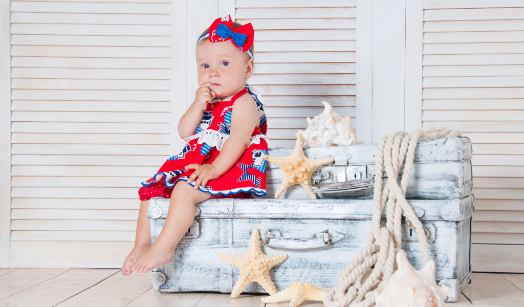 Маленькая девочка сидит на чемодане с морскими звездами