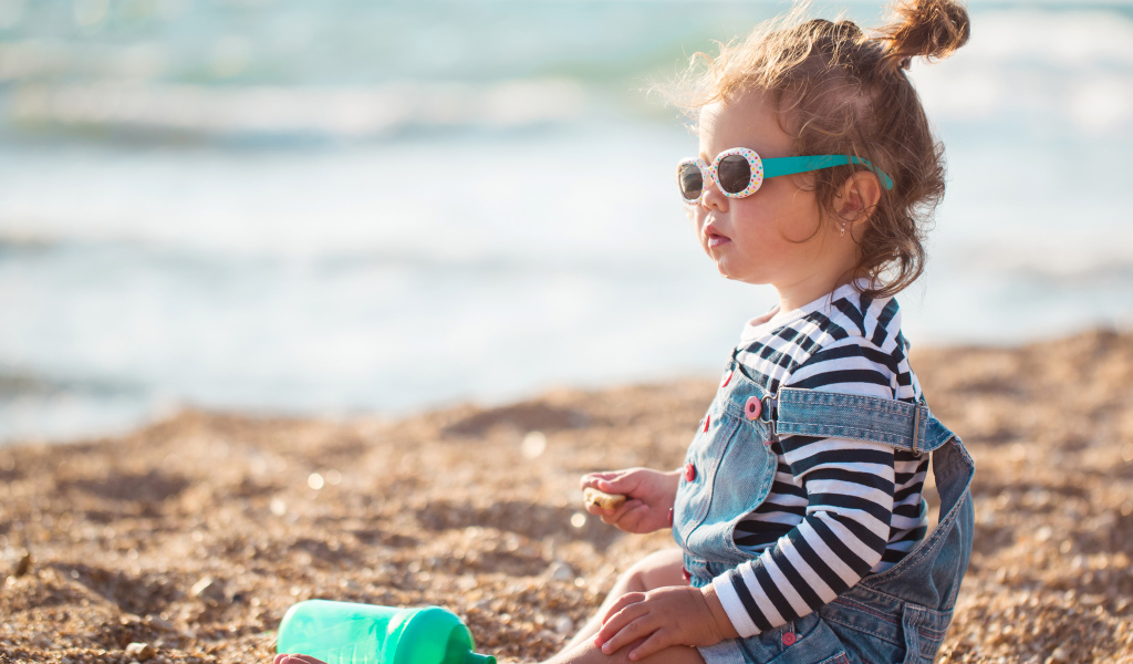 Маленькая девочка сидит на песке на пляже