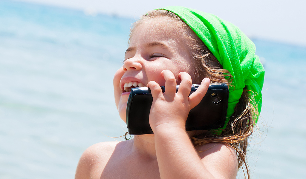Маленькая девочка с телефоном на пляже