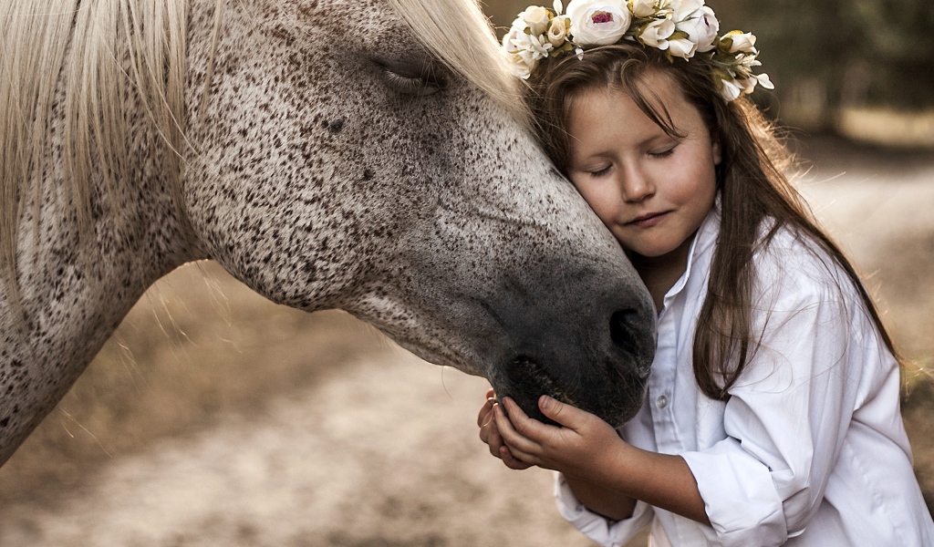 Маленькая девочка с венком на голове обнимает лошадь