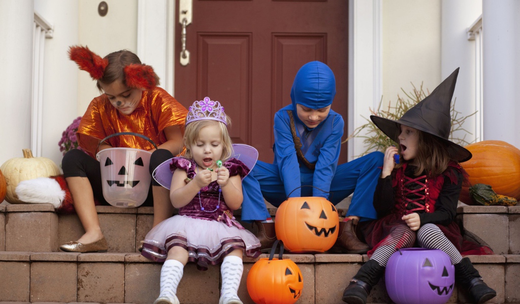 Маленькие дети в костюмах на Хэллоуин сидят на ступеньках со сладостями
