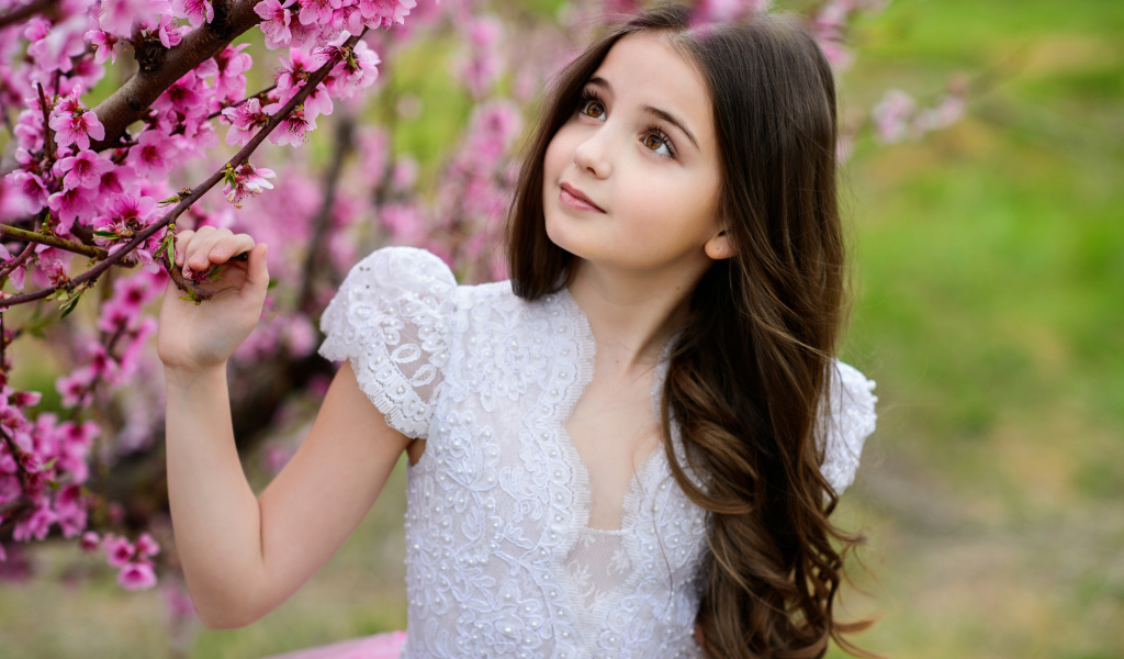 Маленькая длинноволосая девочка у дерева с розовыми цветами