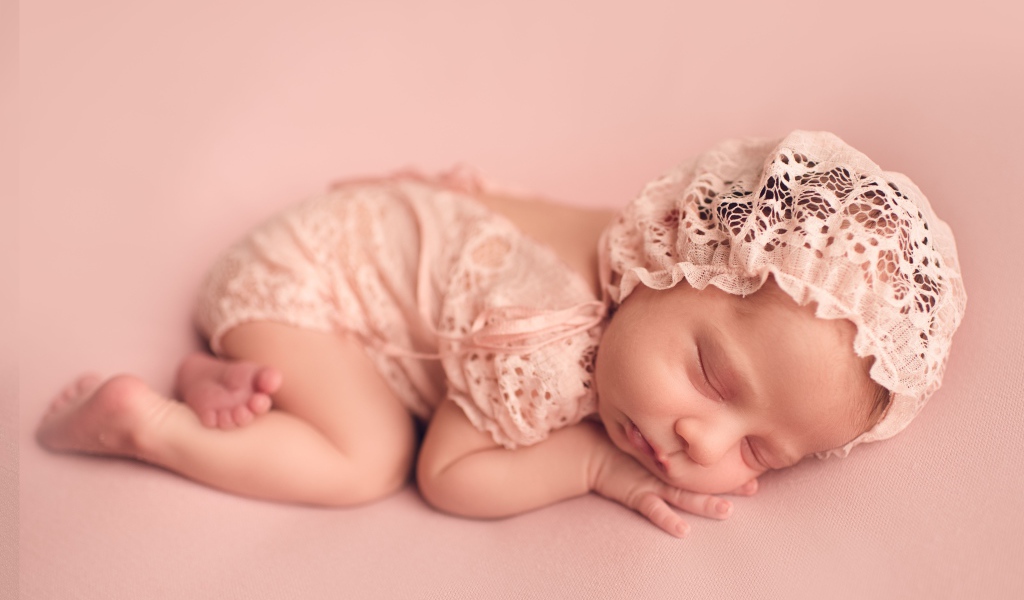 Маленькая новорожденная девочка в розовом костюме 