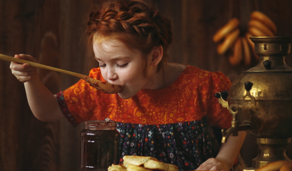 Маленькая рыжеволосая девочка пробует варенье