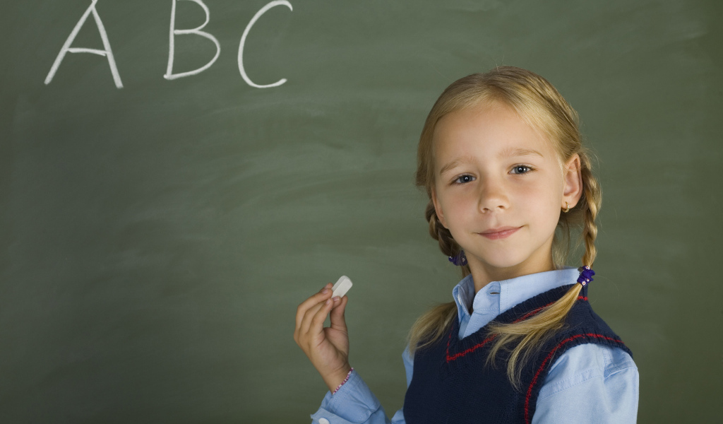 Маленькая школьница пишет буквы на доске 