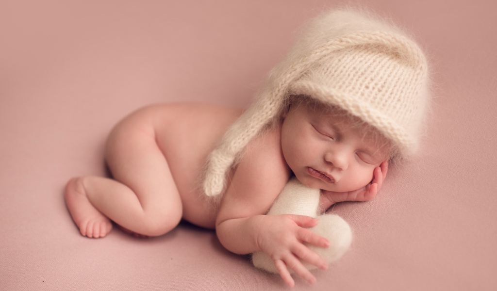 Маленький спящий ребенок в теплой шапке на розовом фоне