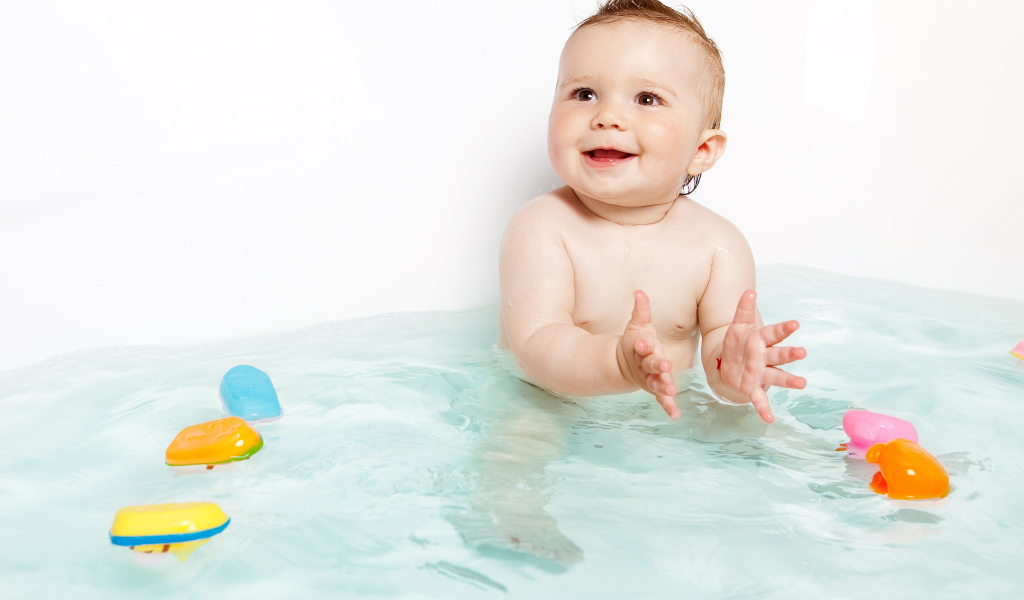 Маленький улыбающийся ребенок с игрушками в ванной 