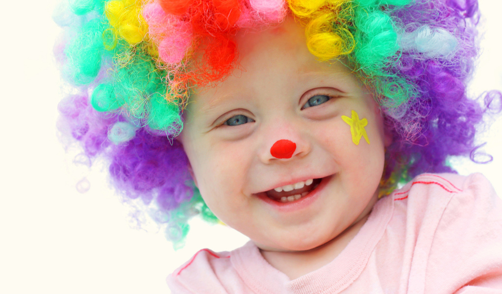 Маленький улыбающийся мальчик в костюме клоуна на белом фоне