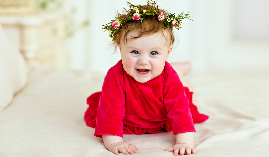 Маленькая улыбающаяся девочка в красном платье с венком на голове