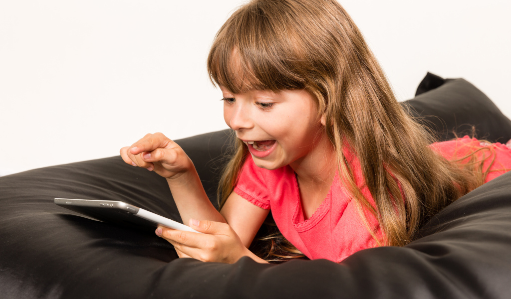 Маленькая улыбающаяся девочка лежит с планшетом