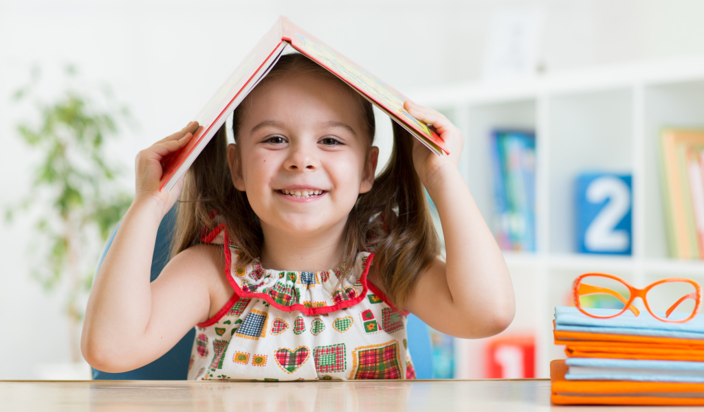 Маленькая улыбающаяся девочка с книгой на голове