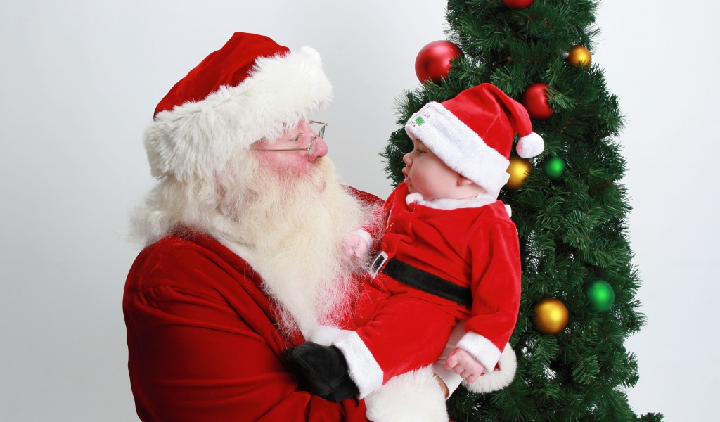 Дед Мороз держит на руках маленького ребенка у елки
