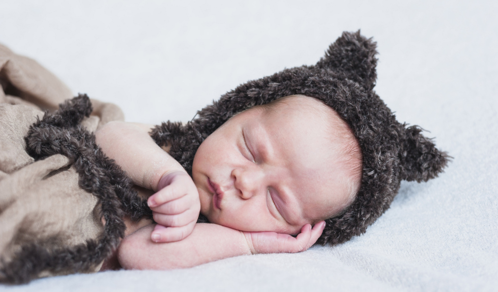 Спящий грудной ребенок в меховой шапке