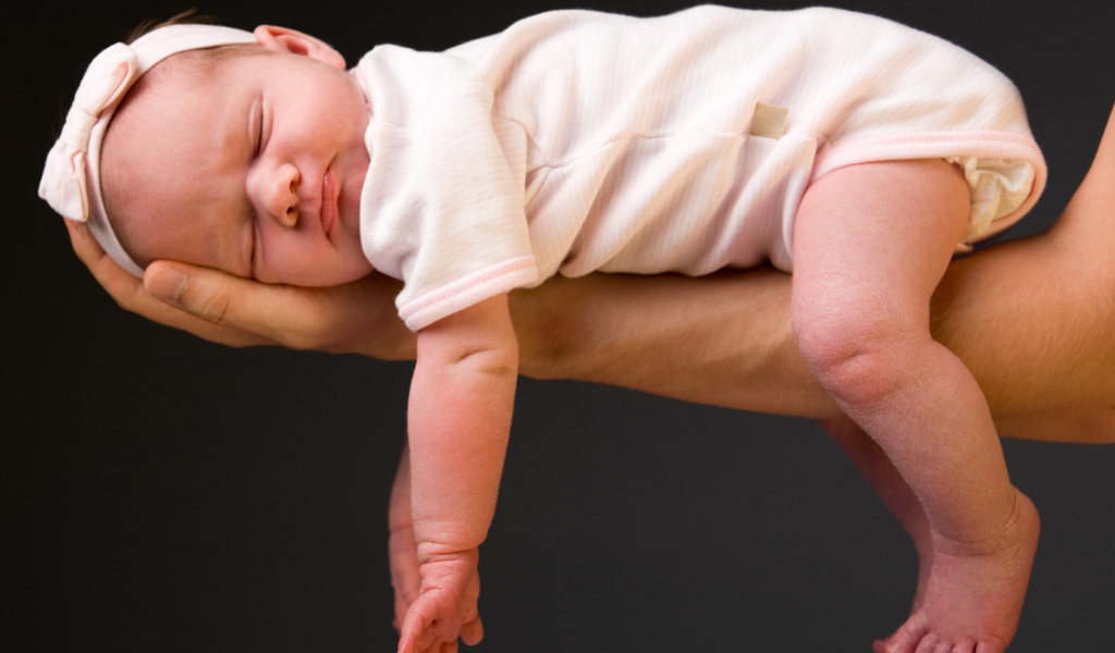 Спящий ребенок на руке у папы на сером фоне