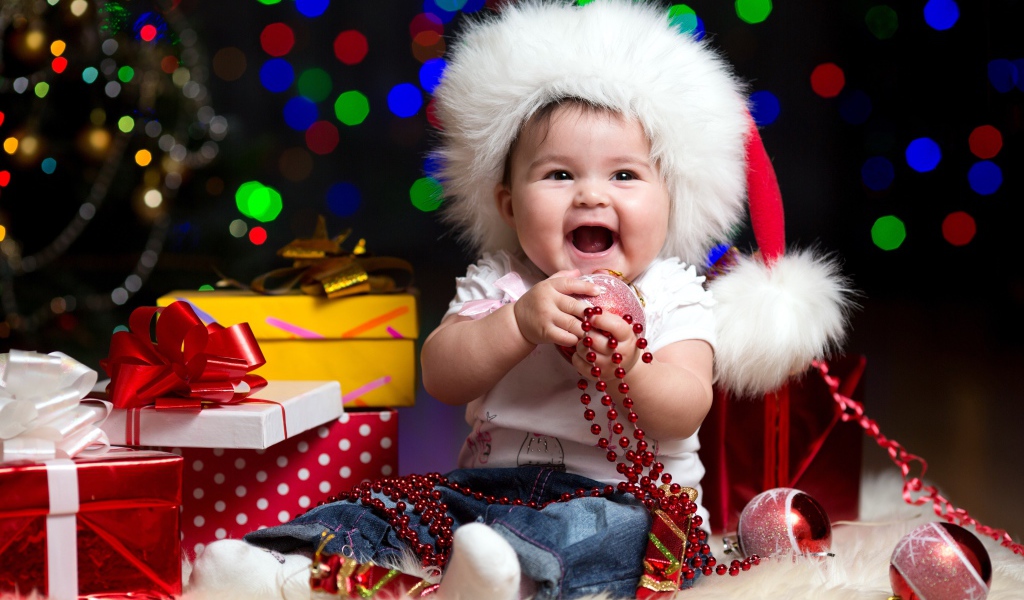 Улыбающийся малыш в новогодней шапке с подарками у елки
