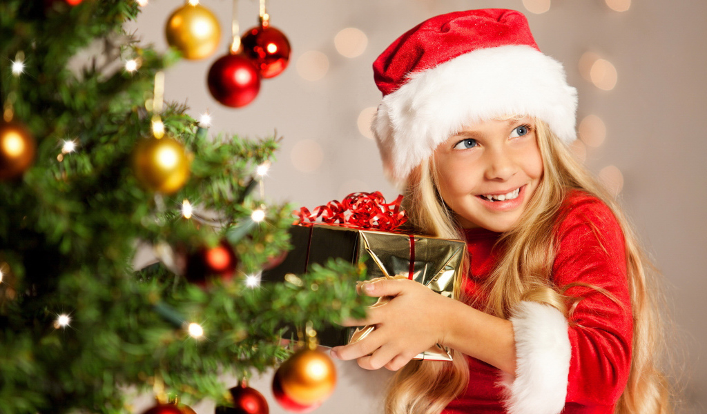 Улыбающаяся девочка блондинка с подарком у елки на новый год 