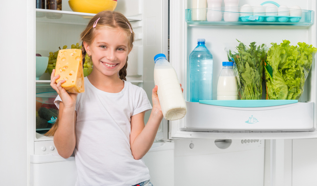 Улыбающаяся девочка у холодильника с сыром и молоком