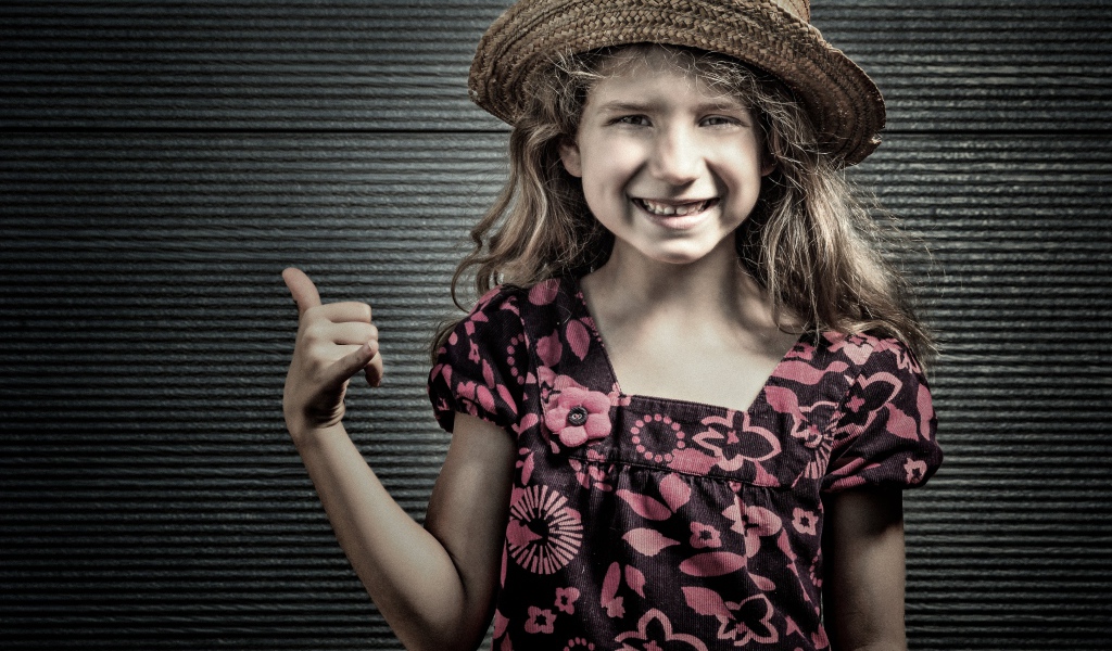 Улыбающаяся девочка в соломенной шляпе у стены 