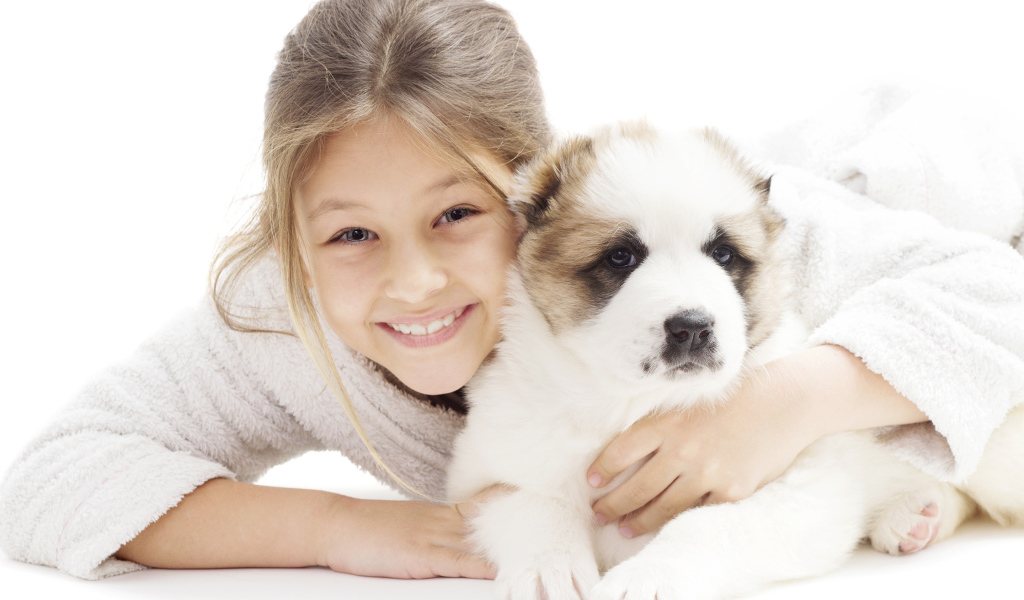 Улыбающаяся девочка лежит с щенком алабая