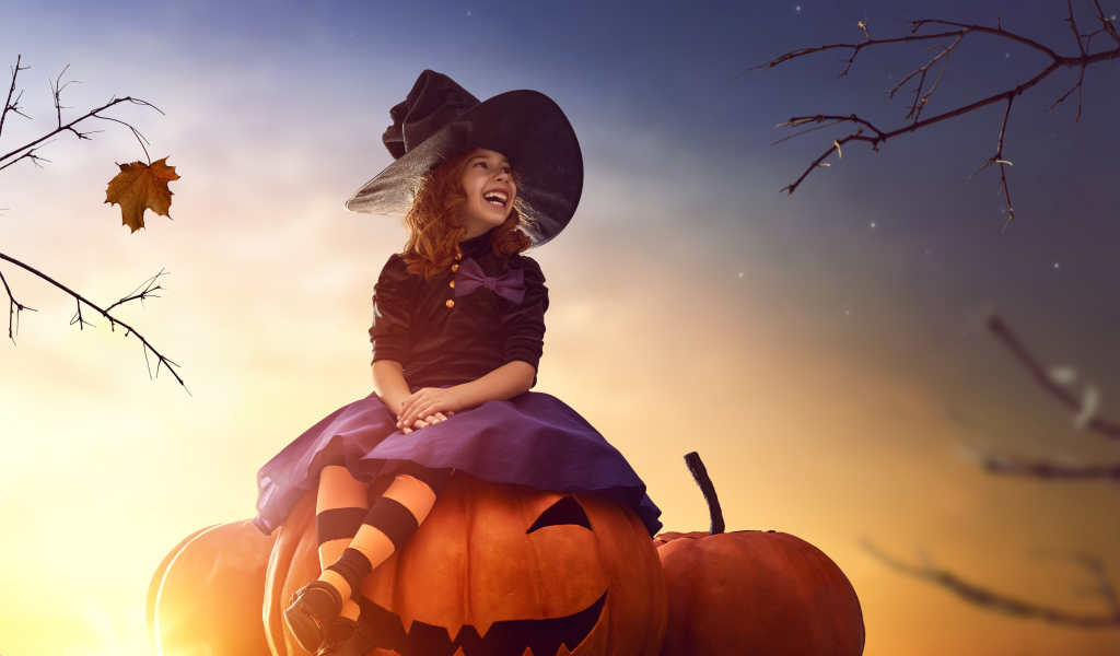 Улыбающаяся девочка сидит на тыкве в костюме на Хэллоуин 