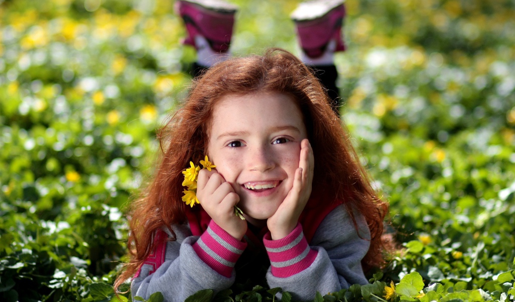 Улыбающаяся рыжеволосая девочка лежит на зеленой траве