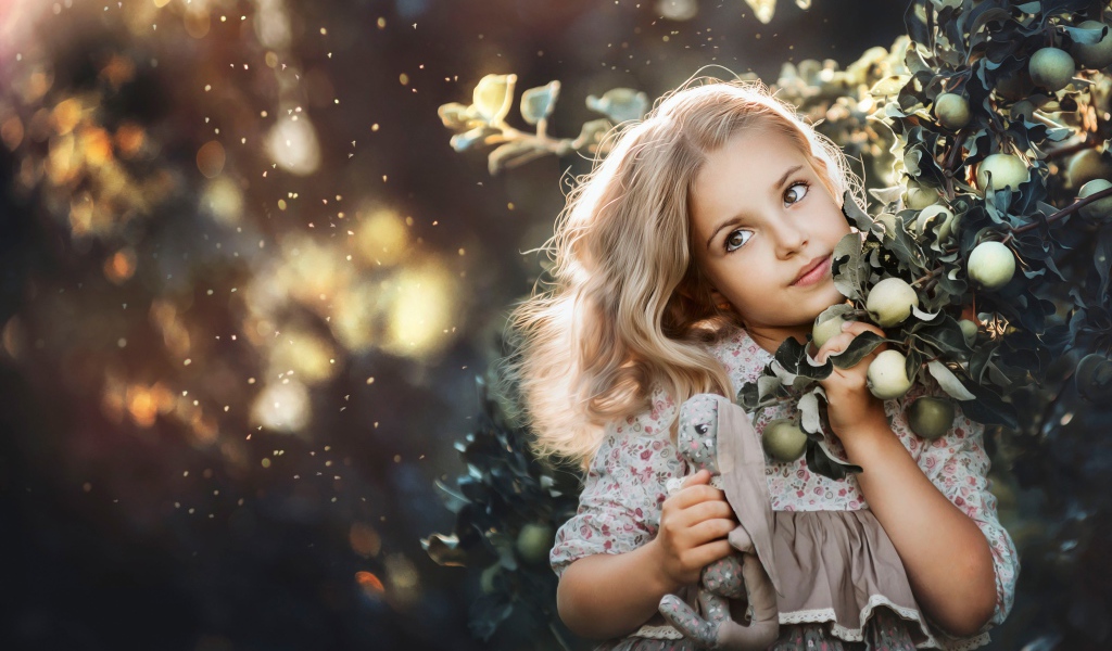 Маленькая девочка стоит у ветки с яблоками