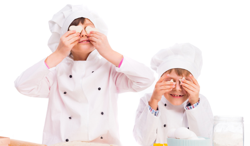 Два маленьких мальчика в костюмах повара на кухне делают печенье