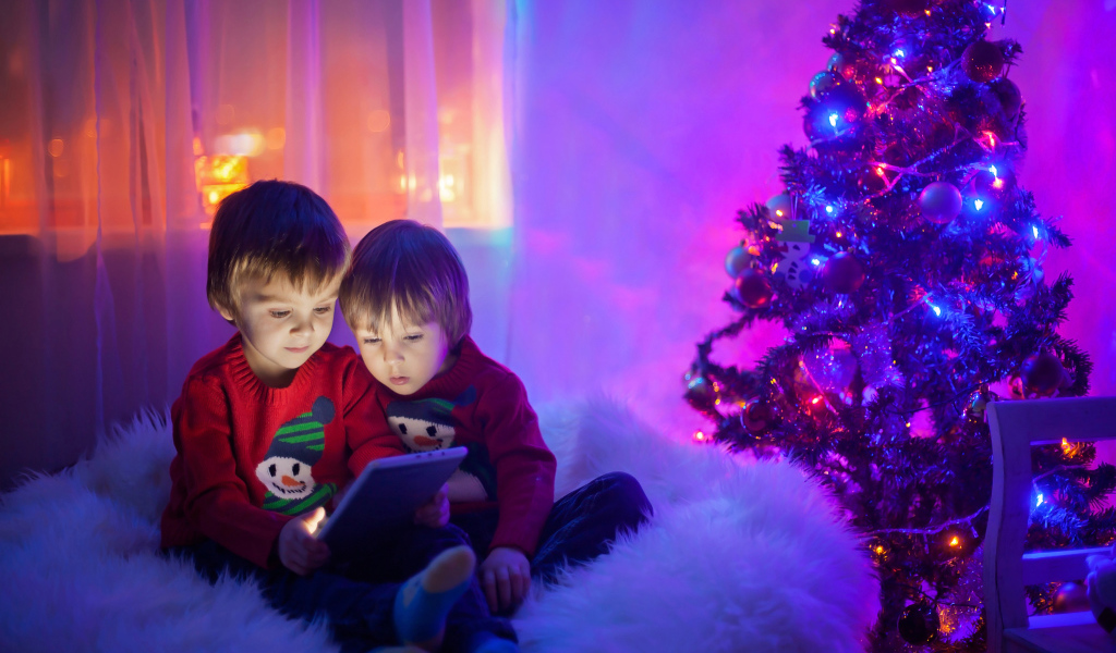 Два маленьких мальчика смотрят мультики у новогодней елки