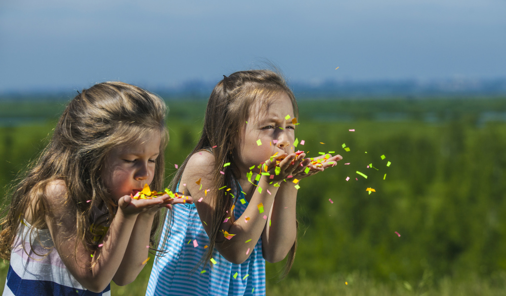 Две маленькие девочки сдувают конфетти  с рук