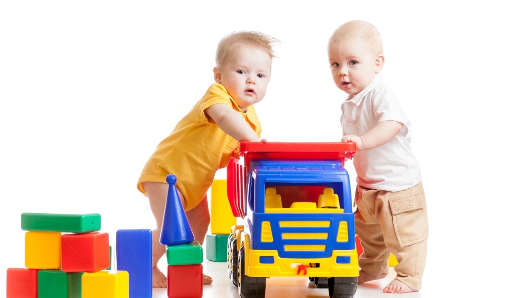 Два маленьких ребенка с игрушками на белом фоне