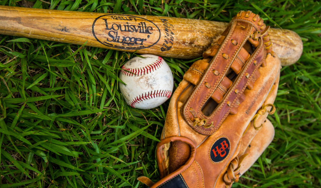 Бейсбольная бита, перчатка и мяч лежат на зеленой траве