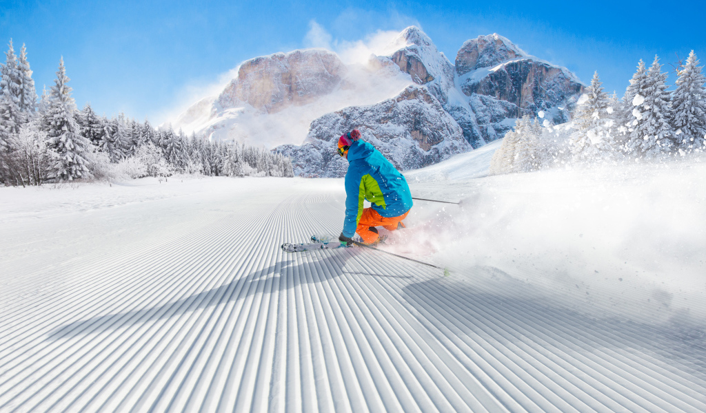 Лыжник спускается по склону на фоне заснеженных гор 