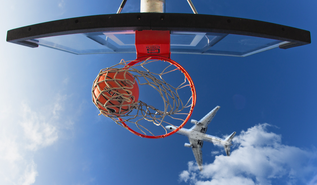 Самолет пролетает над баскетбольным кольцом в голубом небе 