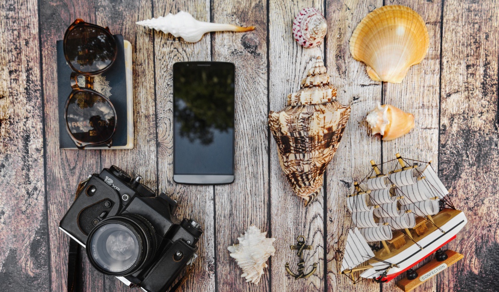 Фотоаппарат, смартфон, ракушки, очки и паспорт на столе