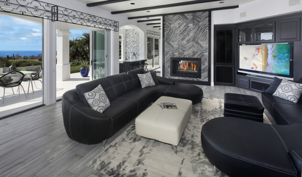 Большая просторная гостиная с черными кожаными диванами, телевизором и камином 