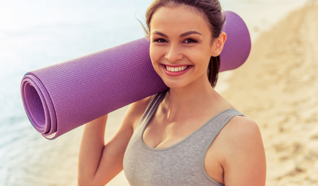 Спортивная девушка с ковриком для йоги на пляже