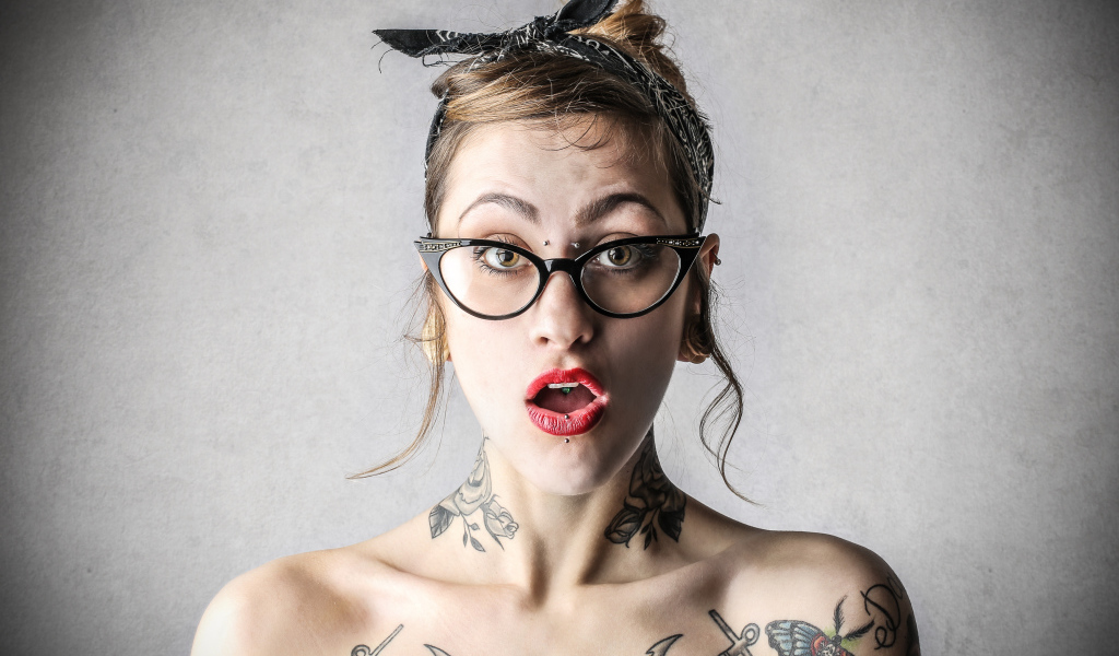 Удивленная девушка в очках с татуировками на теле