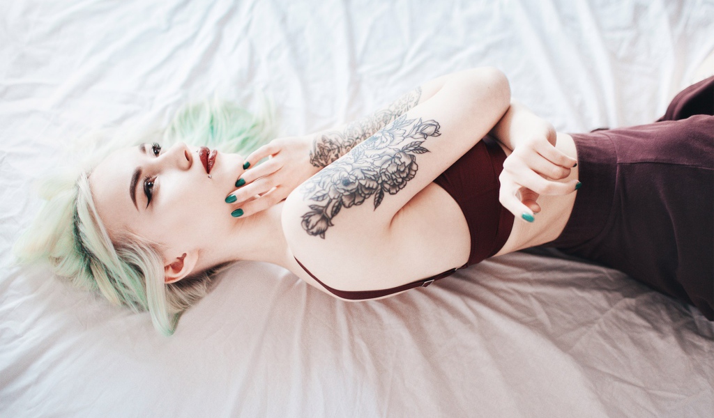 Девушка с татуировкой на руке лежит на кровати 