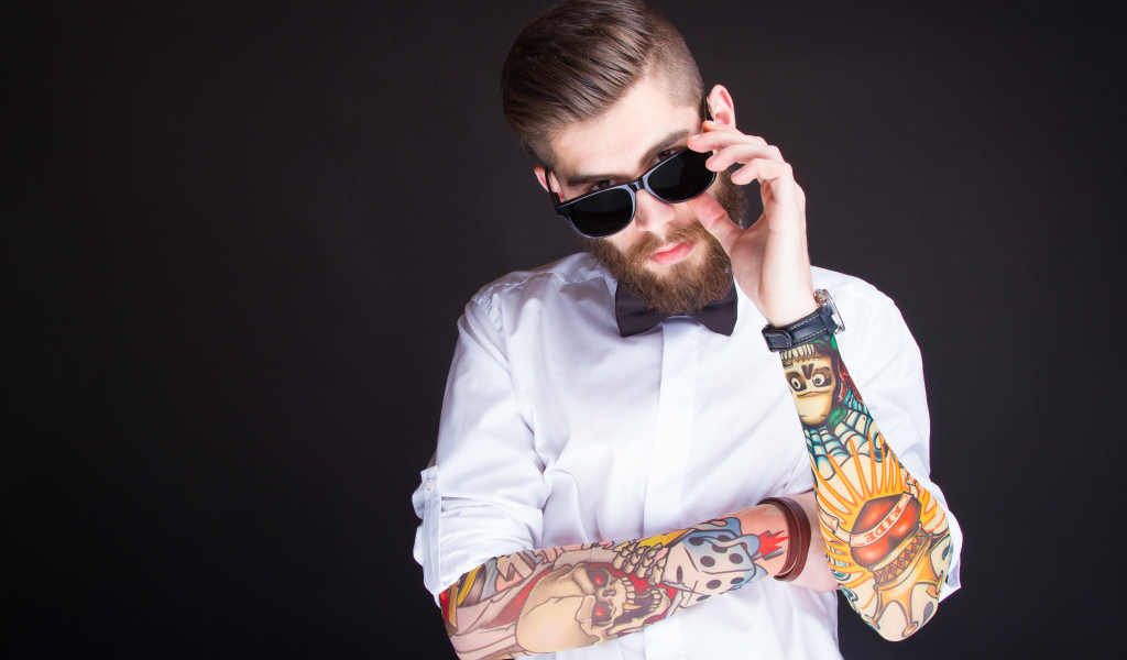 Мужчина в очках с татуировками на руках на сером фоне