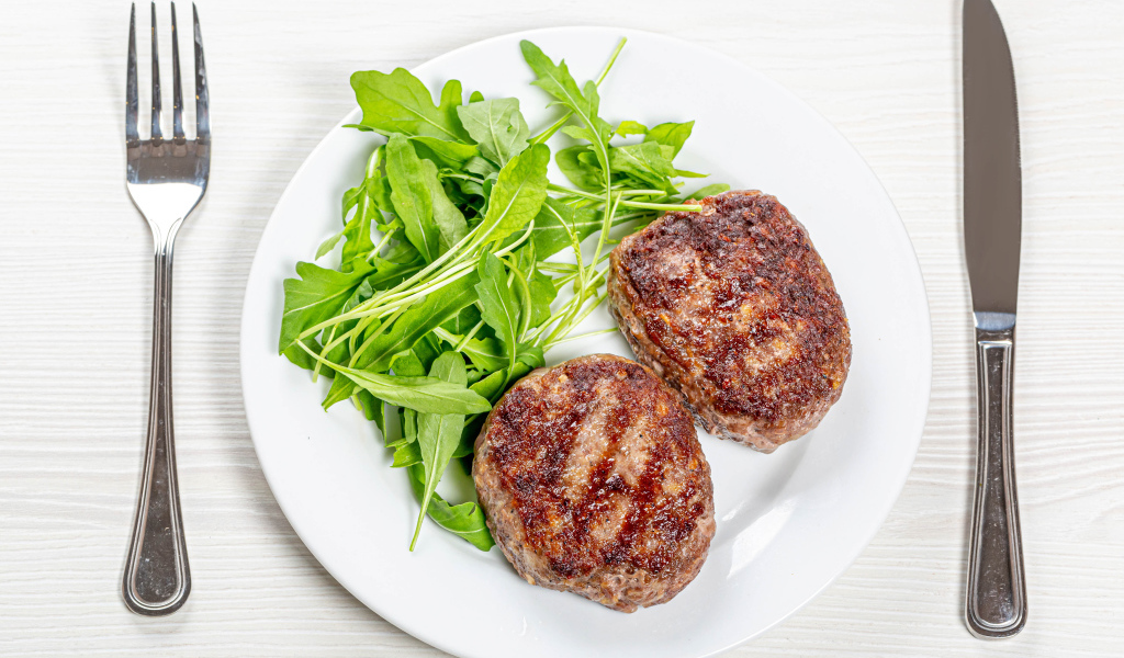 Две котлеты на тарелке с зеленью рукколы 