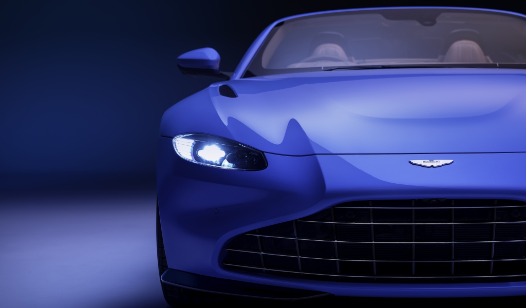 Синий автомобиль Aston Martin Vantage Roadster 2020 года с включенной фарой 